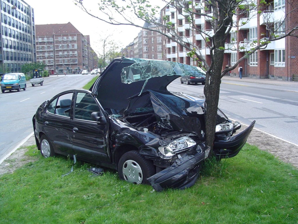 Banged up black car head on collision with tree