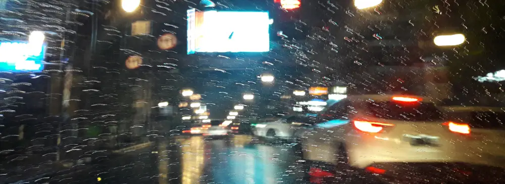 Photo from inside a car in the city at night with rain on the windshield and traffic outside