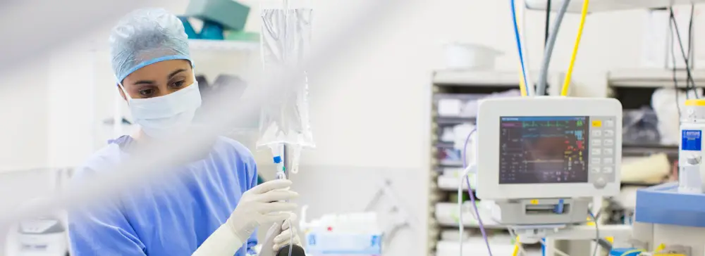A nurse with an IV bag standing in an operating room with medical equipment